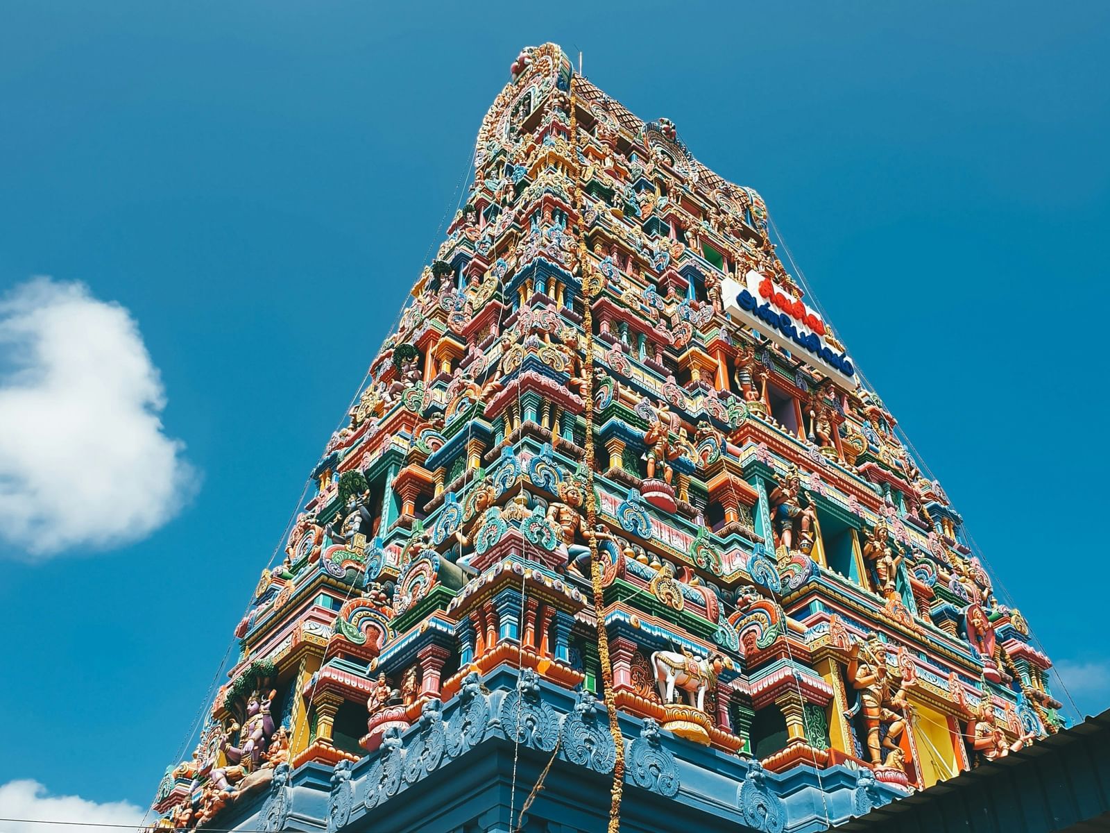 A south Indian temple gopuram, adorned with intricate carvings and vibrant colours, standing tall against a clear blue sky.