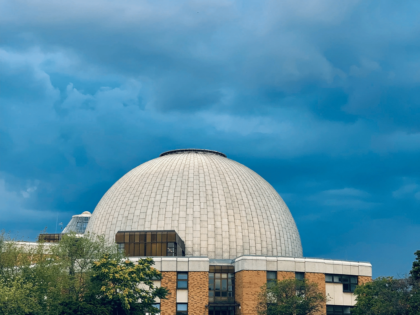 Modern dome-shaped structure set against a dramatic cloudy sky.