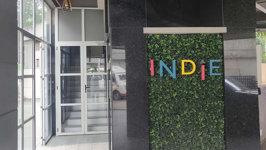 A plant backdrop with Indie in sleek metal text gracing a wall in the corridor at Indie Stays, BKC Kalina.