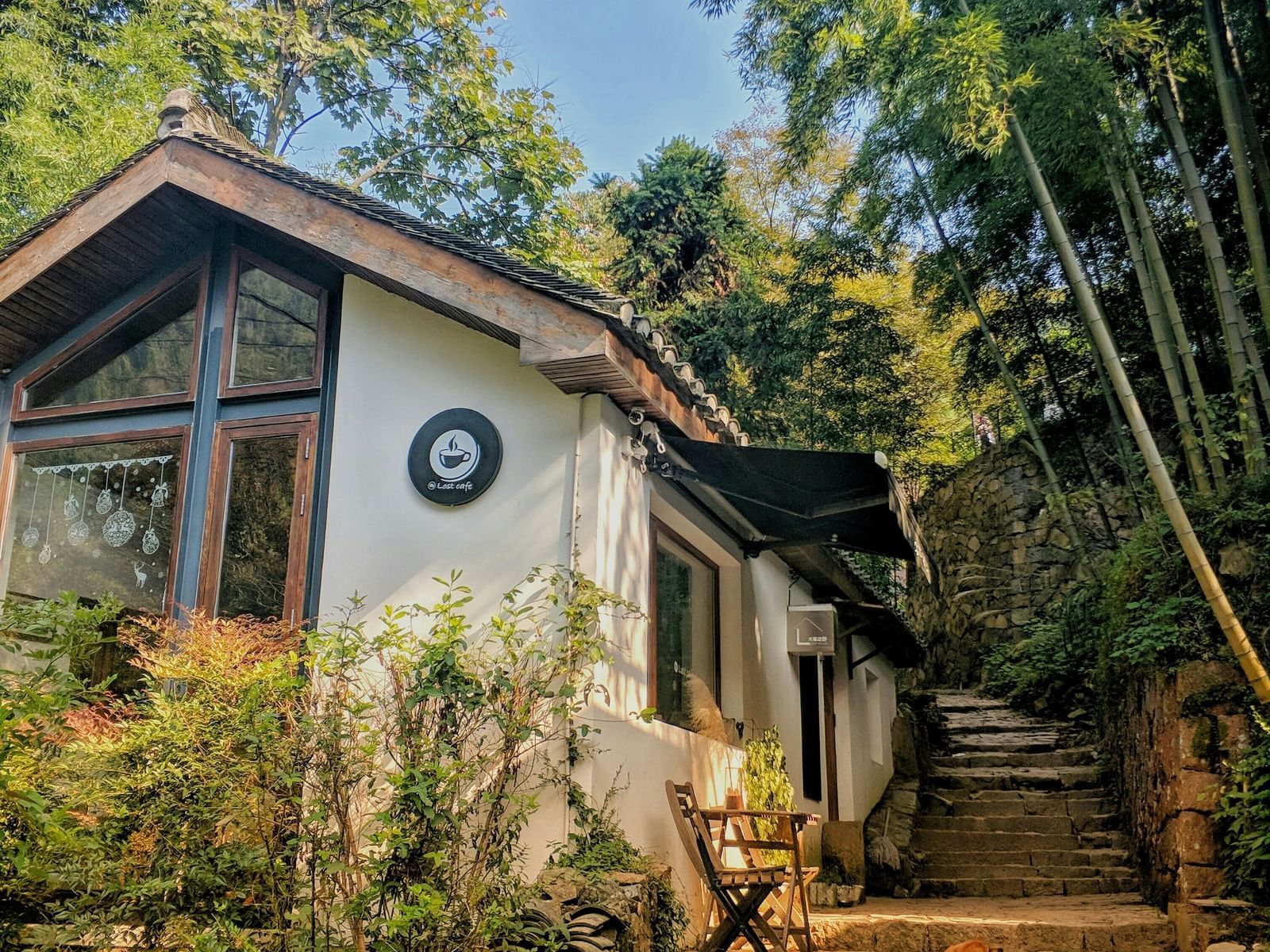 A charming white house with a brown roof nestled among green trees and a stone staircase.