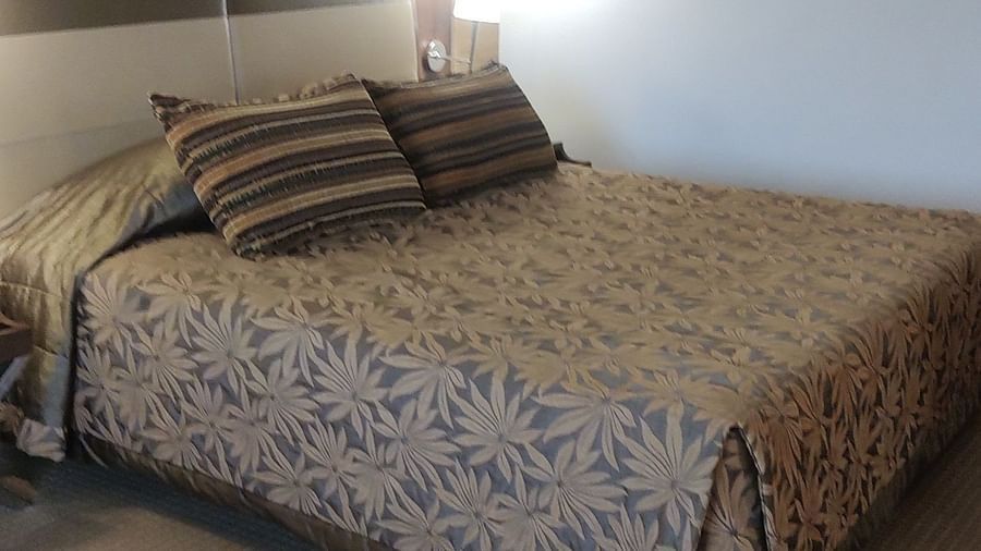 A hotel bedroom featuring a patterned bedspread, matching pillows, and framed floral artwork above the headboard - The Retreat Hotel and Convention Centre