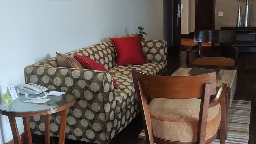 A living area featuring a patterned sofa, side table with a phone, a wooden chair, and framed floral artwork on the wall - The Retreat Hotel and Convention Centre