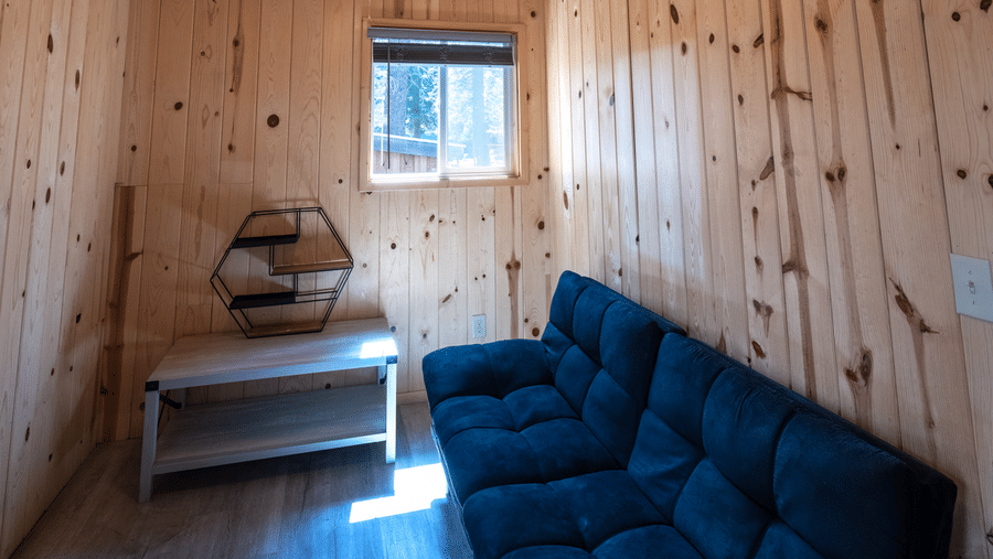 A sitting area at Kit Carson Lodge with a cushioned sofa, wooden side table, and a window allowing natural light into the space
