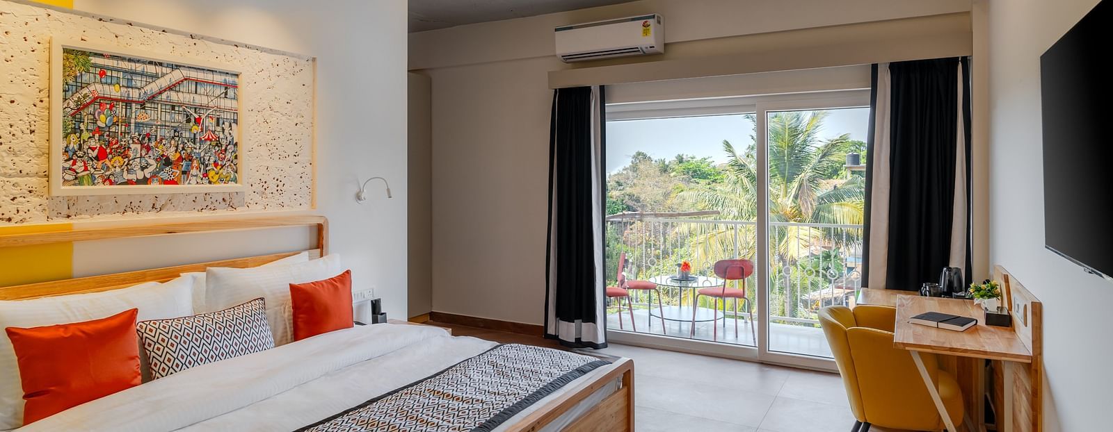 Bright hotel room with, flat TV screen, work desk and chair, vibrant art on the wall, and an access to the balcony at Bedzzz Xclusiv Morjim, Goa