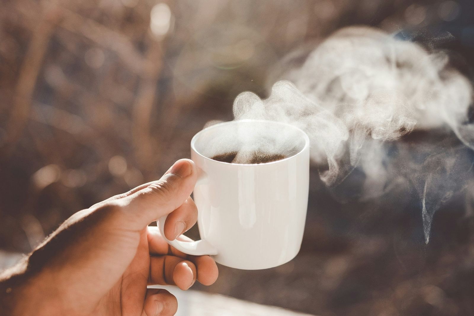 Image of a person holding a steaming cup of coffee