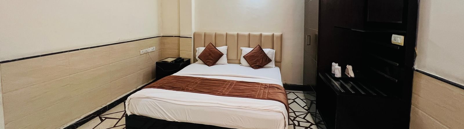 A well-furnished hotel room featuring a comfortable bed with red pillows and dark wood furniture, offering a restful stay. | Suite | Hotel Aadhar