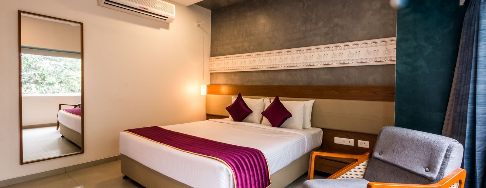 A spacious hotel room featuring a large bed, a full length mirror, and a comfortable armchair at Shilton Dee Cee.