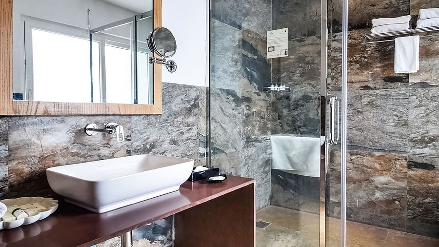 A modern bathroom with a glass shower, a wash basin on a dark counter, and a large mirror.- Bamboo Saa Resort & Spa, Udaipur