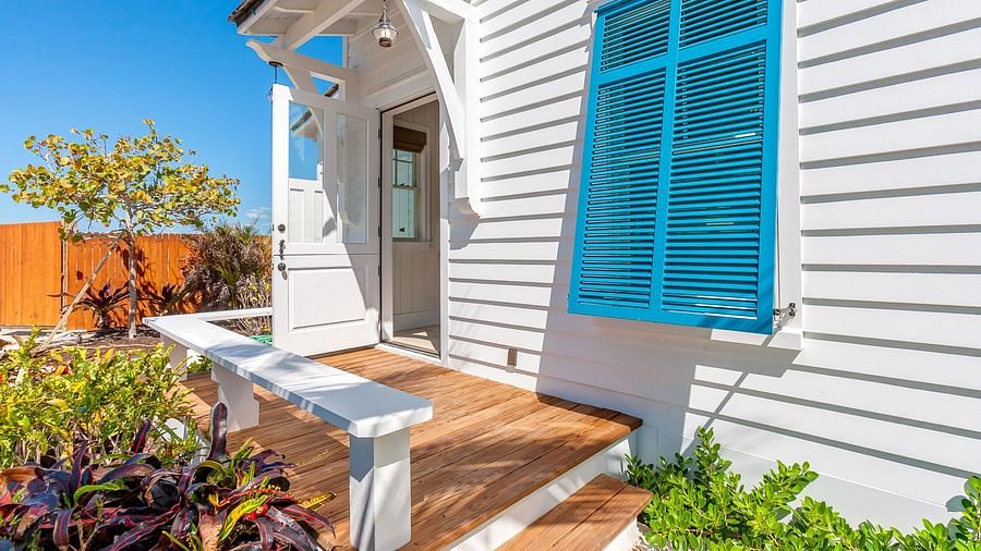Side patio with a wooden bench, blue shutters, and lush greenery | Abaco Inn