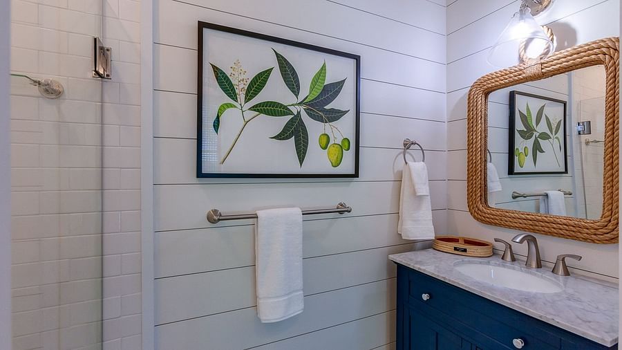 Bathroom with a navy blue vanity, gold-framed mirror, white walls, and botanical artwork above towel racks | Abaco Inn