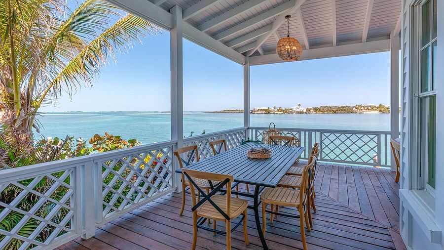 Outdoor dining area on a wooden deck with white railings, overlooking the blue sea and tropical surroundings | Abaco Inn
