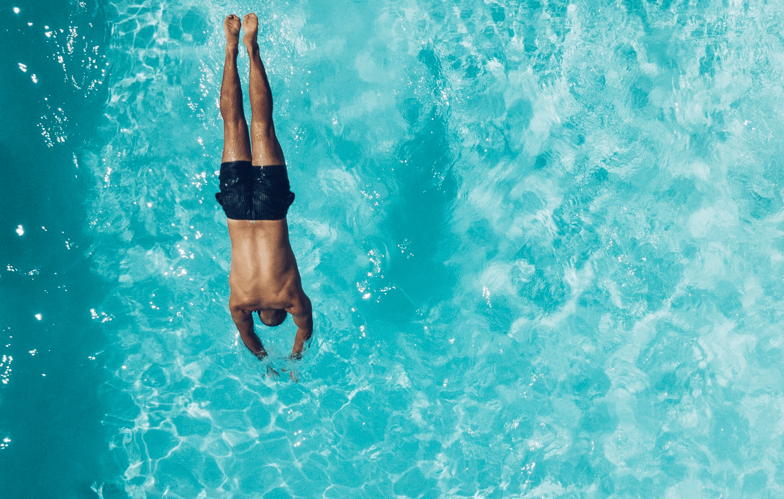 An overhead shot of a person swimming in a clear, turquoise outdoor swimming pool.