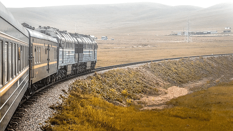 A train running over the tracks with vast grasslands on both sides of the track.