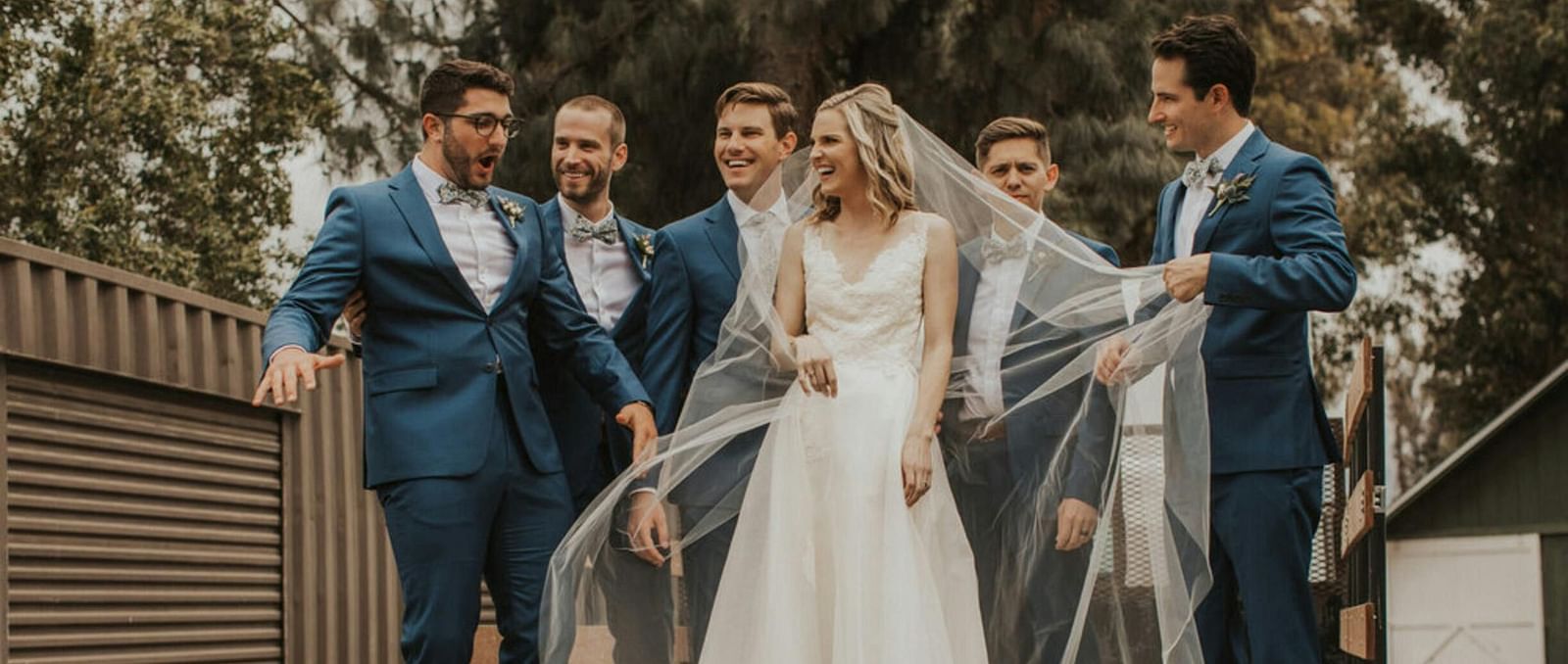 A bride posing for a photo with the groomsmen on a wooden patio
