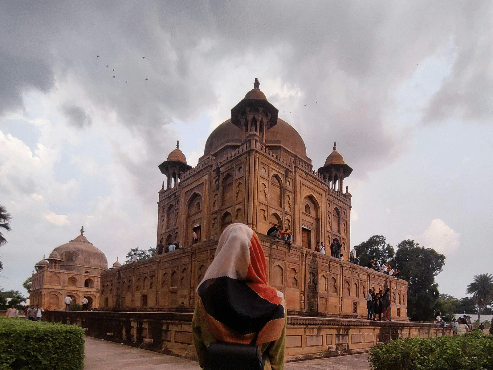 A person in a yellow and black outfit standing in front of an old, reddish-brown building with unique architectural features.