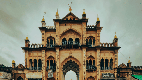 A large, ornate building with a central archway is reflected in a pool of water in front of it.
