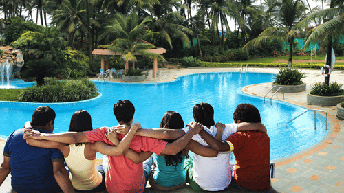 A group of six people sitting together by the edge of a large swimming pool with palm trees in the background at The Retreat Hotel & Convention Centre.
