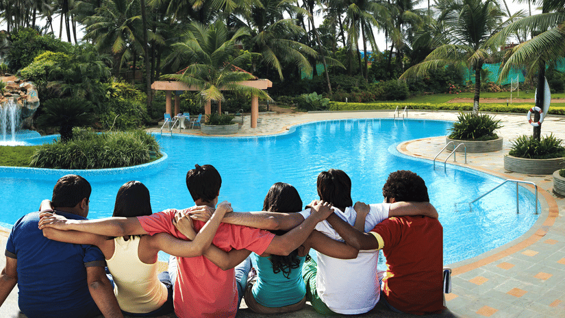 A group of six people sitting together by the edge of a large swimming pool with palm trees in the background at The Retreat Hotel & Convention Centre.