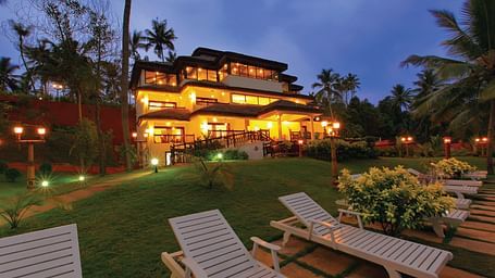 A grand building surrounded by a lush, expansive lawn with three beach beds positioned in the foreground, evoking a serene and inviting atmosphere - Fragrant Nature Kollam