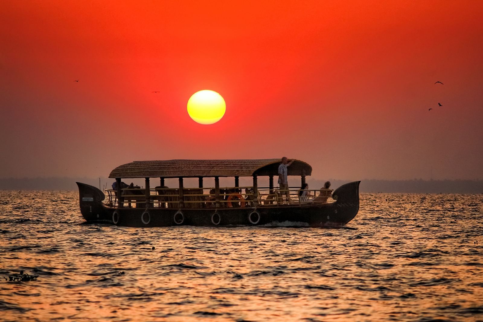 a solitary boar travelling on a lake in Kumarakom with the sun setting in the background