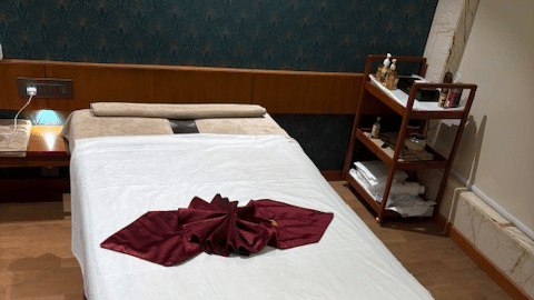 A professional massage table neatly prepared with white linens and a decorative maroon runner - Praveg's Grand Eulogia, Ahmedabad