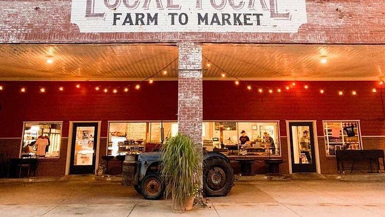 Exterior view of a market place named local yocal farm to market with a red wall on the outside and fairy lights as  decoration.