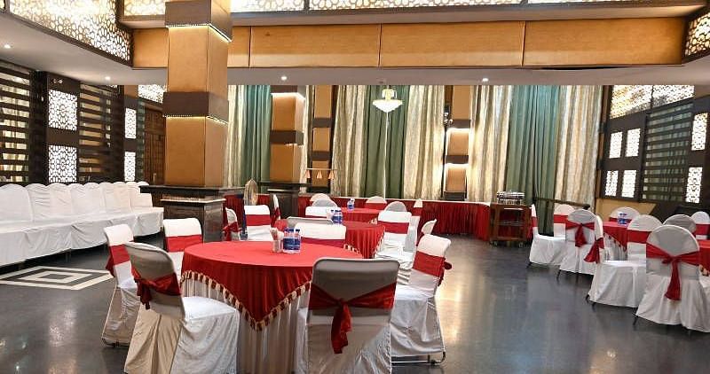 A beautiful conference hall with elegant lights in the ceiling featuring round tables set up all across the hall at Hotel Gold, Panipat.