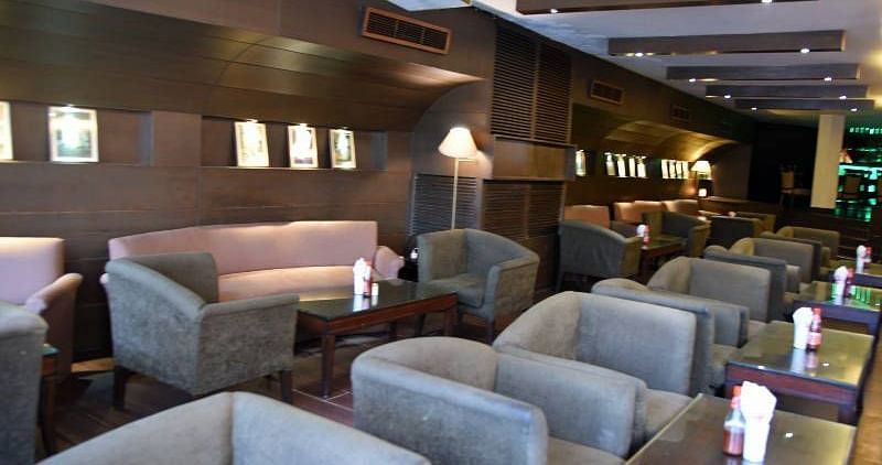 Several grey coloured cushioned arm chairs placed in front of individual tables with a projector hanging from the ceiling at 24 Karats Bar - Hotel Gold, Panipat