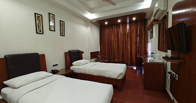 A bedroom with two single beds and dark wooden flooring along with a wall mounted television - Hotel Gold, Panipat