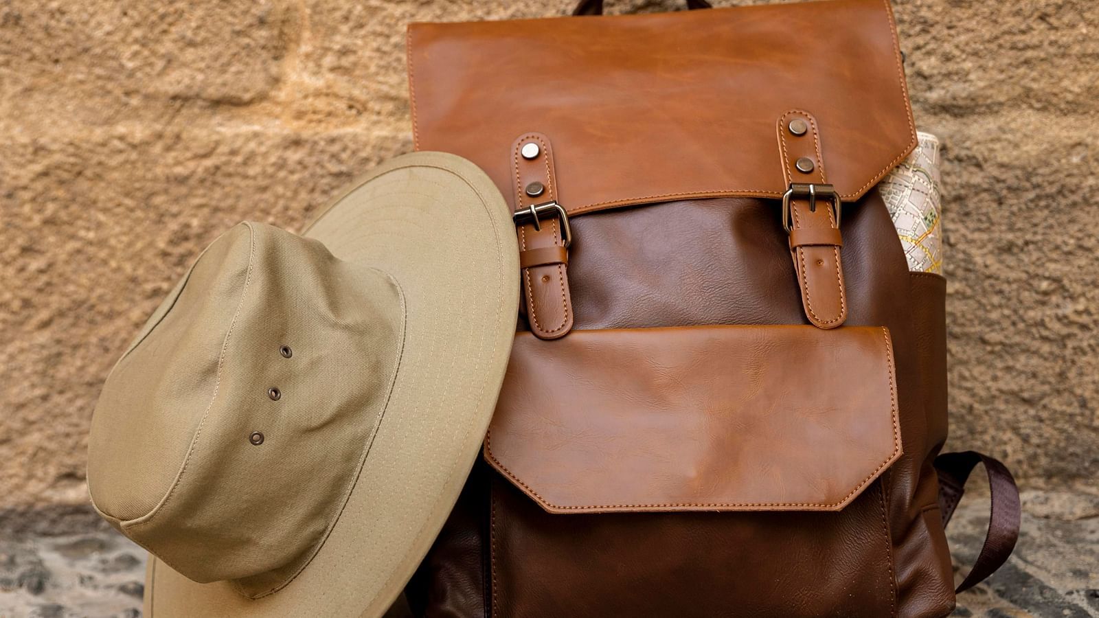 Safari backpack and wide-brimmed hat resting against a textured stone wall, ready for an outdoor adventure