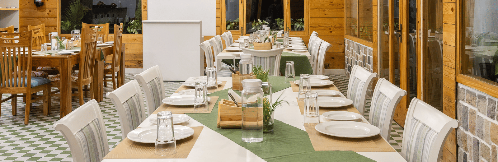 An intimate dining room setting with wooden walls, a television screen, and a long table ready for guests - Megha Resort & Villas, Dehradun