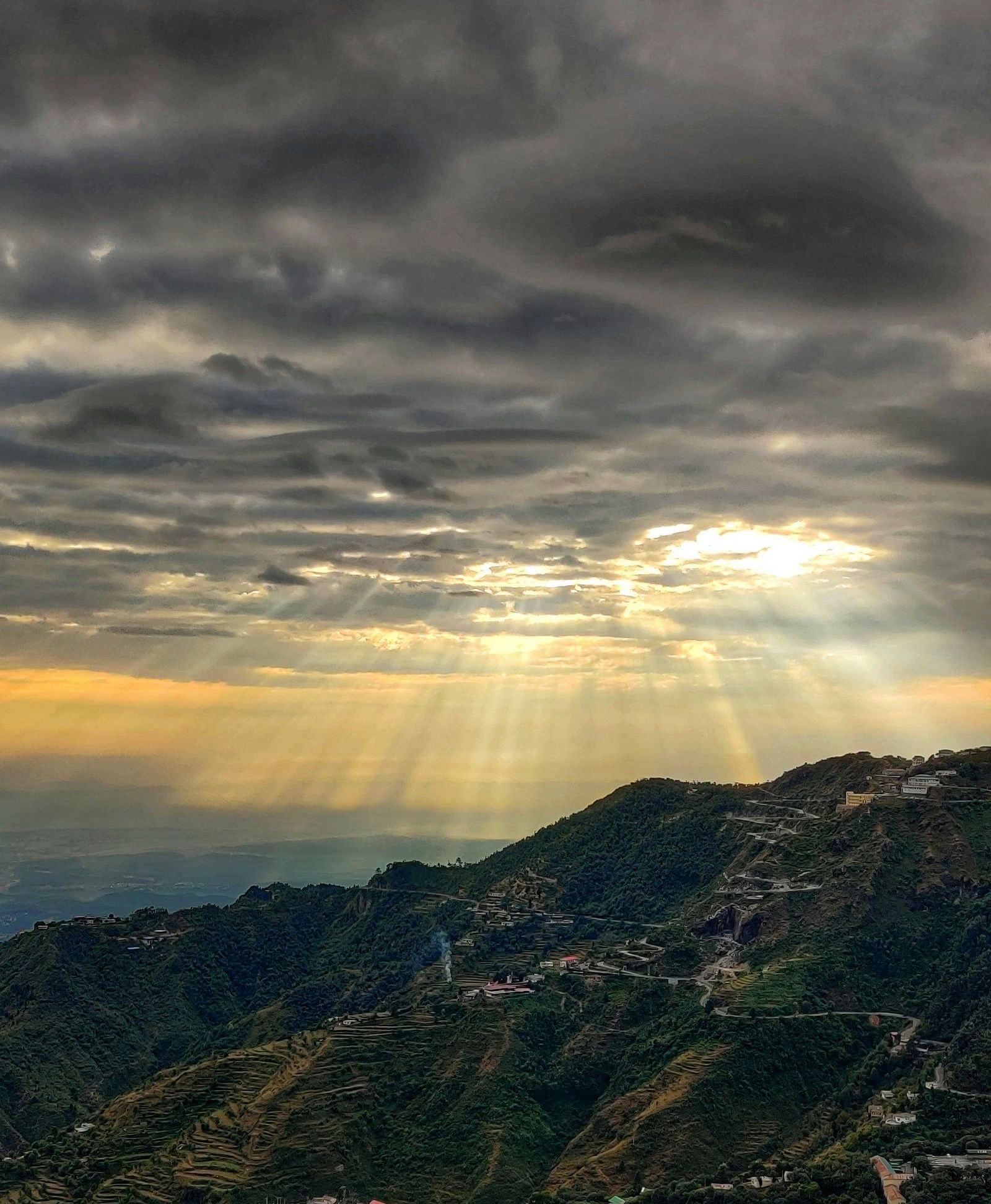 Sun rays breaking through storm clouds over terraced mountain slopes