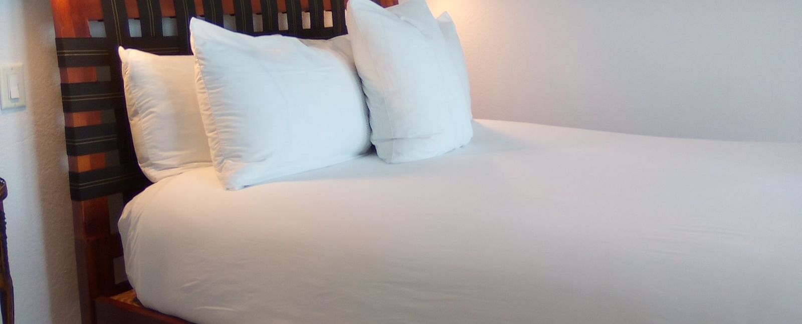Bed with white linens and wooden headboard at Casa Morada, shown from a side angle.