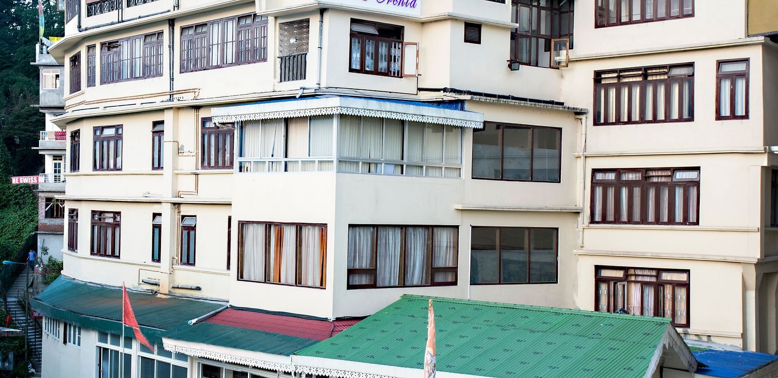 The exterior of New Orchid Lords Inn Gangtok  is shown during the daytime, nestled on a hillside with multiple stories and windows.