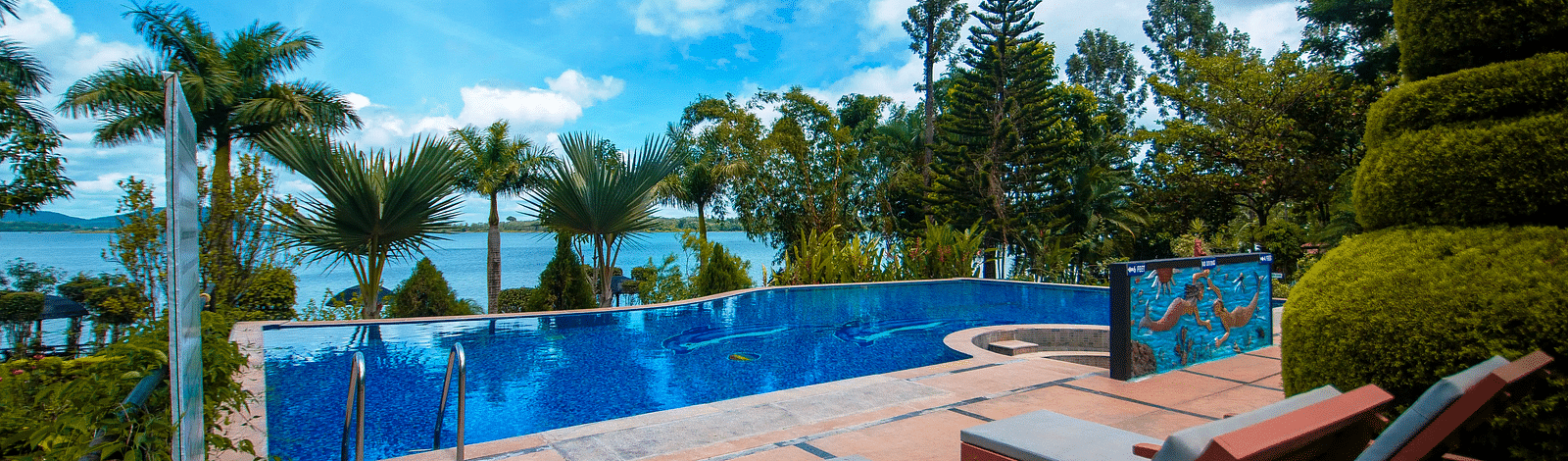 A swimming pool with sun loungers on the side at Coorg Jungle Camp Backwater Resort, Kushalnagar.