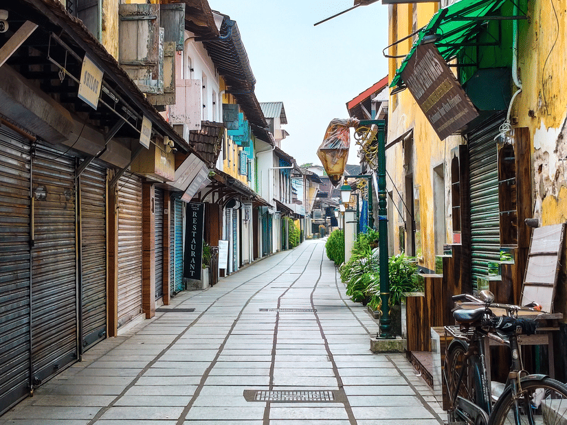 A charming heritage lane lined with colourful buildings, shops, cafés, and traditional architecture creates a vibrant street scene.