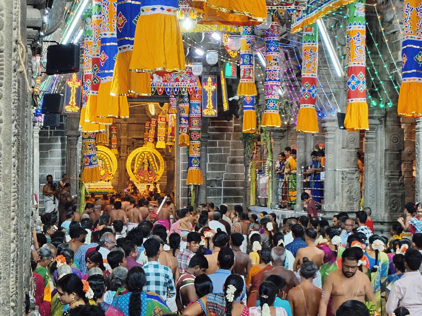 Crowd of devotees gathered inside a brightly decorated Hindu temple corridor during a religious festival or event.