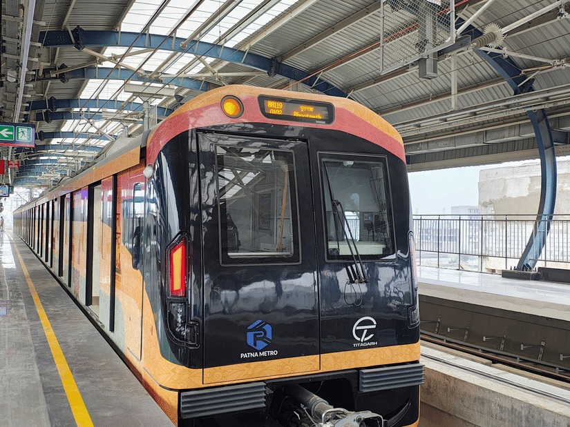 A modern metro train arriving at an elevated station platform under a curved steel roof structure.
