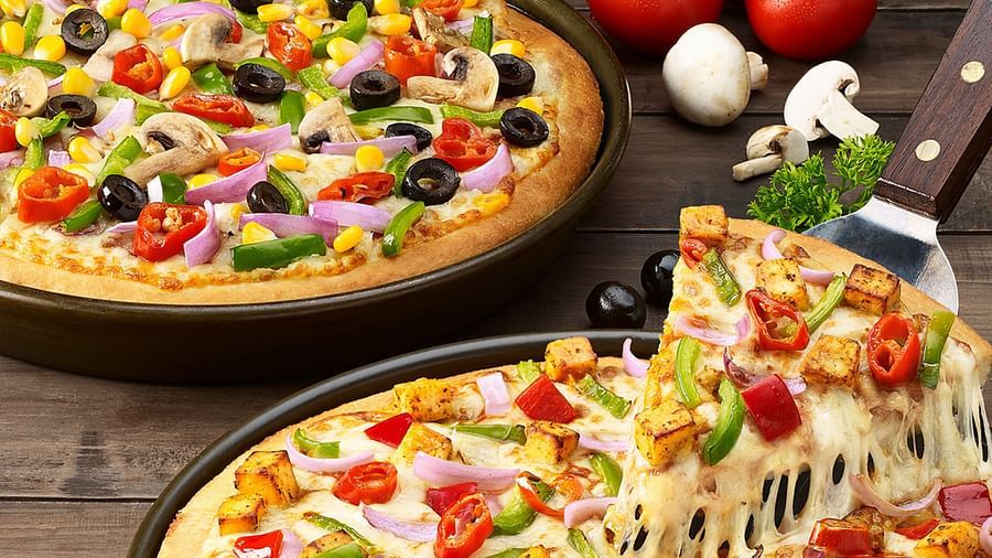 A cheesy pizza loaded with fresh vegetables and sliced, being lifted to show the stringy cheese - Themis Barbecue House, Ambience Mall, Gurugram
