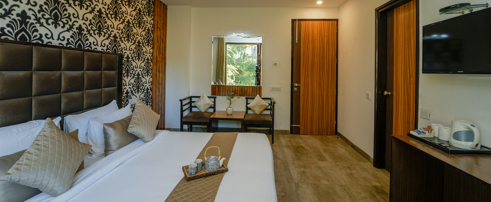 An image of the deluxe room with a bed, chairs and table, flat screen TV, and other room amenities - DLS Whispering Winds