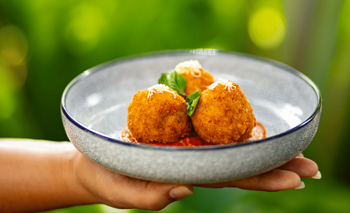 A person holds a plate with three fried, golden-brown appetisers on a bed of red sauce at Stanley Revelation.