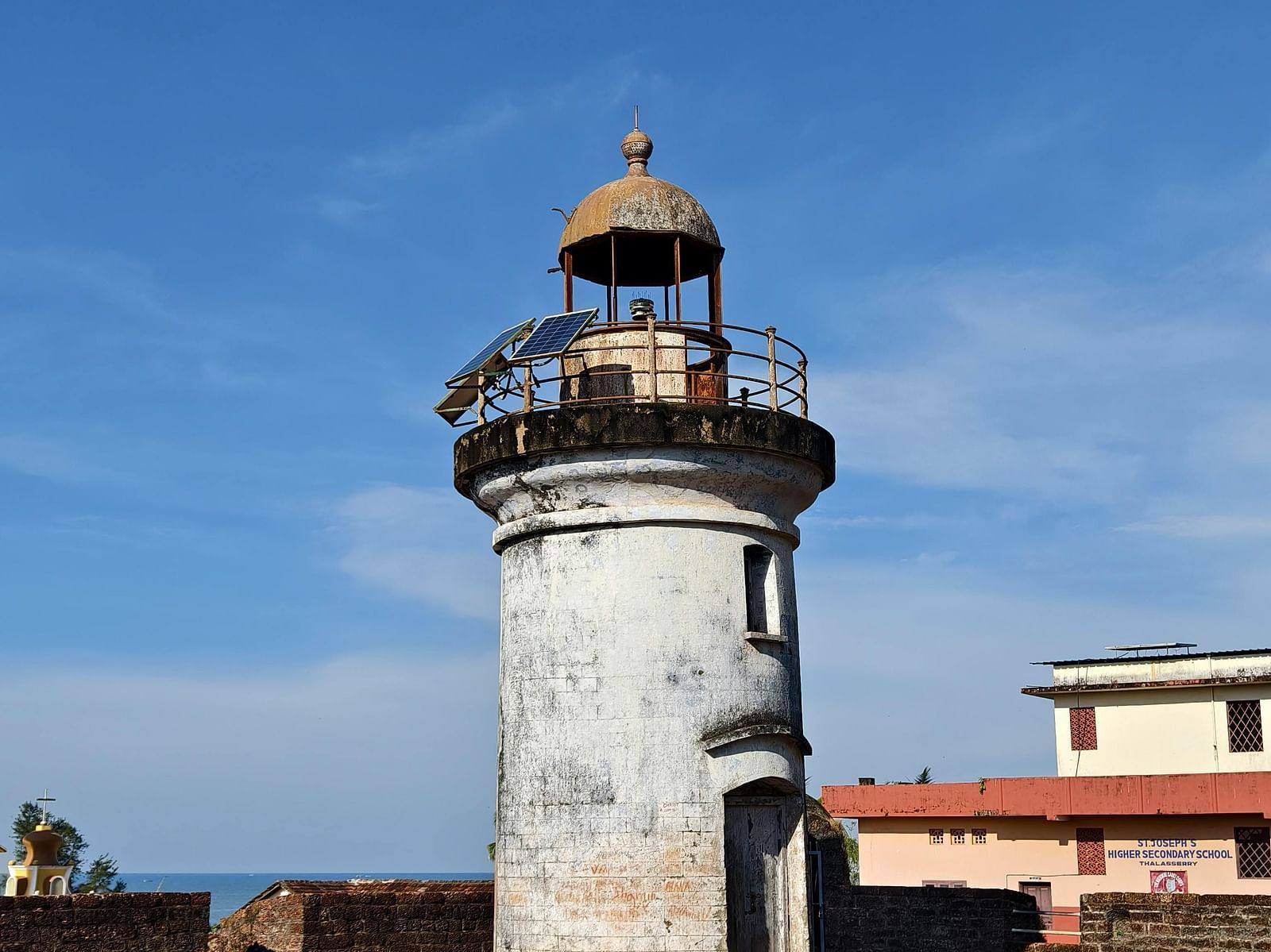 A tall, historic lighthouse with a white facade and black lantern room, standing against a clear blue sky.