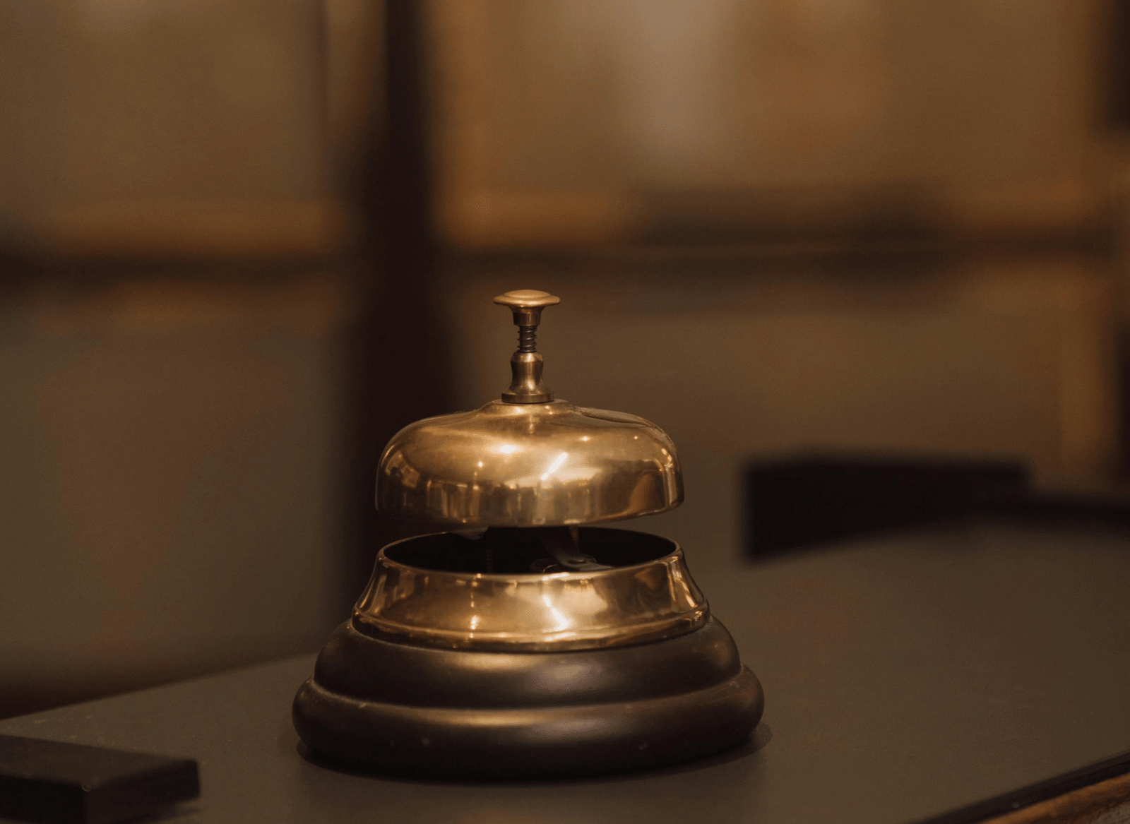 A close-up of a brass reception bell resting on a dark wooden surface, slightly blurred.