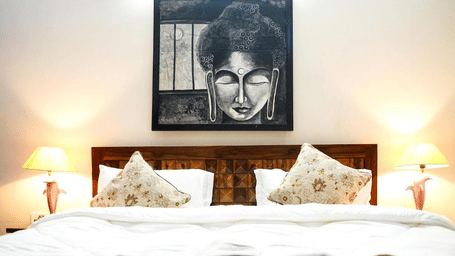 Bedroom of Lime Tree Hotels & Service Apartment Private Limited featuring a framed portrait artwork, white bedding, and bedside lamps.