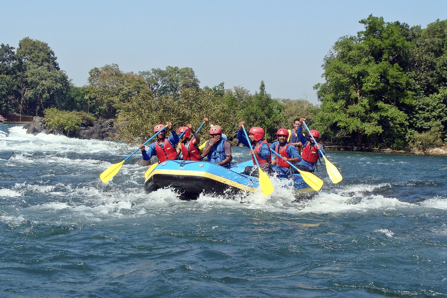 A group of adventurers in life jackets, joyfully rowing together in their raft on a scenic river, surrounded by nature.