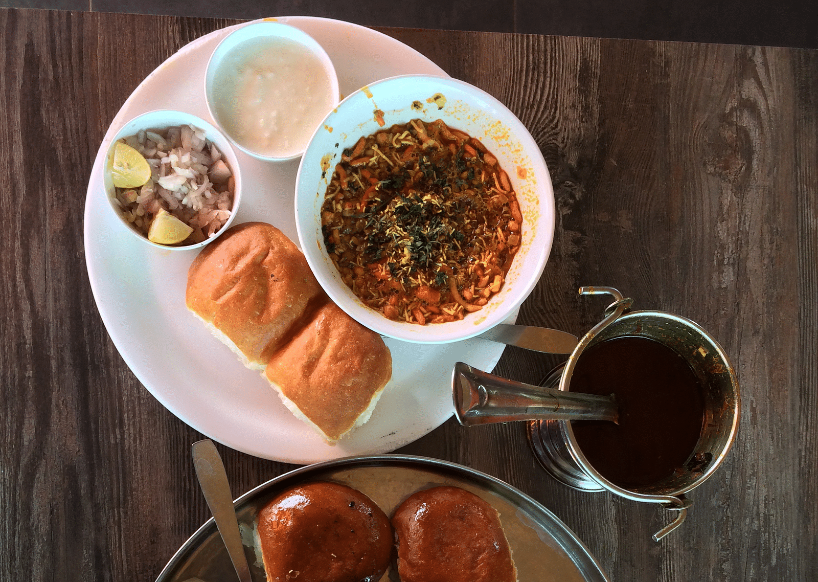 An aerial view of a breakfast spread that includes misal pav with onions, curd and other items.