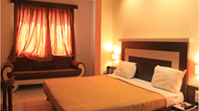 Cozy hotel room with warm ambient lighting, a double bed, and a wooden sofa set beneath a window with brown curtains.