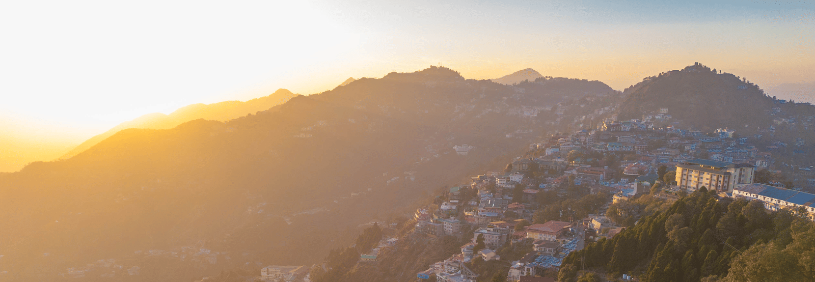 A panoramic view of a mountain town built on rolling hills, bathed in the golden light of sunrise or sunset | Perfectstayz Value Valley Vista