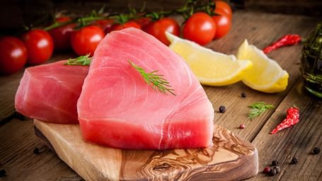 Fresh tuna steak on a wooden board, garnished with herbs and surrounded by lemon and tomatoes.