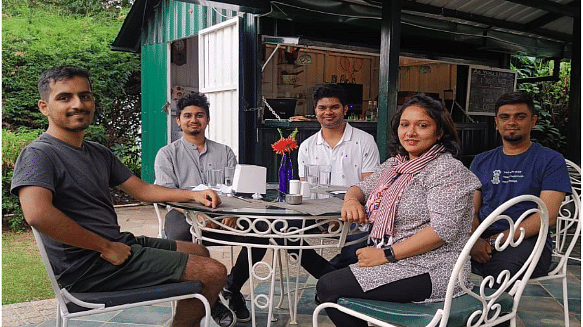 Small group of guests enjoying drinks at a round outdoor table under a shaded patio.